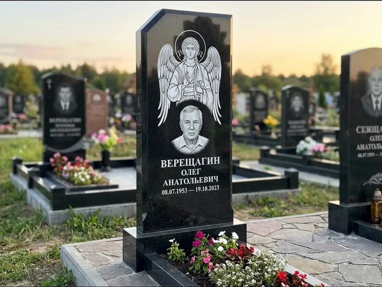 Памятник с гравировкой иконы: стела с резным навершием и нимбом в золоте — гравировка образа Спасителя, высокие разросшиеся туи полукругом, работа «Мельникова» в Кемерово