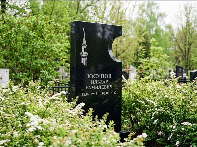 Мусульманский памятник с гравировкой мечети: стела с боковым вырезом в форме полумесяца — гравировка минарета с полумесяцем, низкие кусты спиреи в цвету, работа «Юсупов» в Кемерово